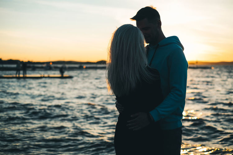 Couple embracing while standing against sea during sunset
