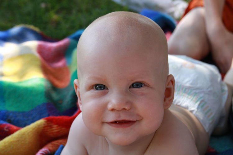 Close-up portrait of baby boy smiling while lying on blanket at field