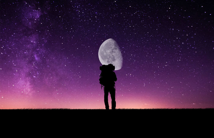 Silhouette hiker standing against moon with star field at night