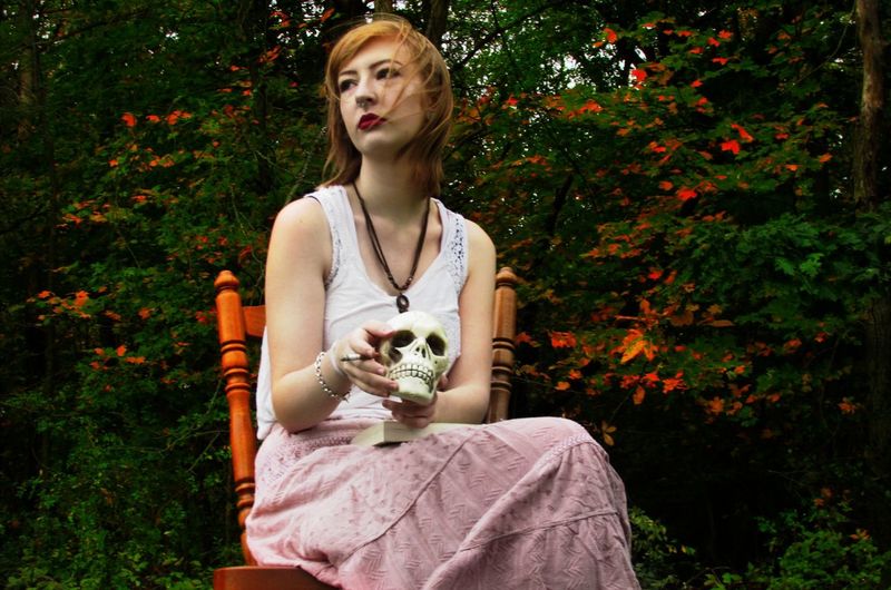 Young woman sitting with artificial skull and cigarette