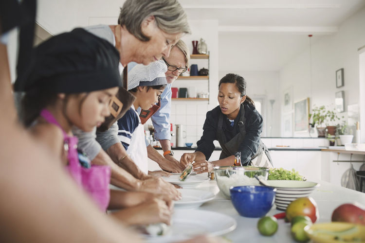 Woman guiding family in preparing food at kitchen