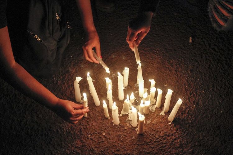 Cropped image of people igniting candles at night
