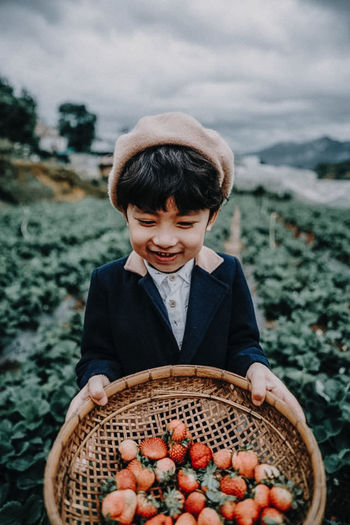 Boy holding basket with strawberries at farm