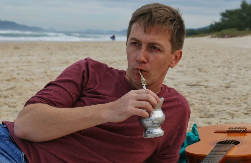 Young man drinking yerba mate while relaxing at sandy beach