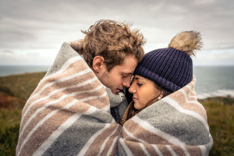 Couple covered with blanket romancing by sea on field