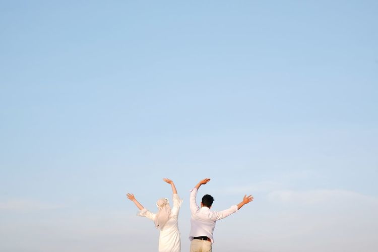 Rear view of woman with arms raised against clear sky