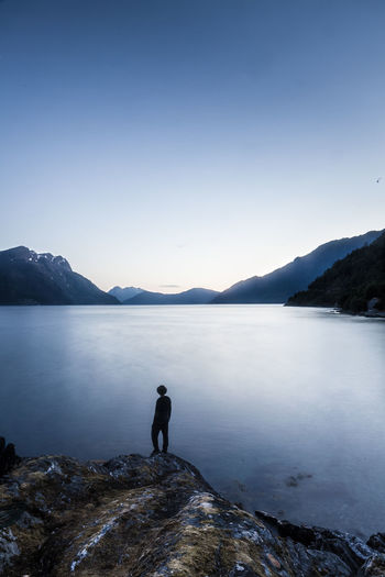 Silhouette man standing on cliff by lake against sky