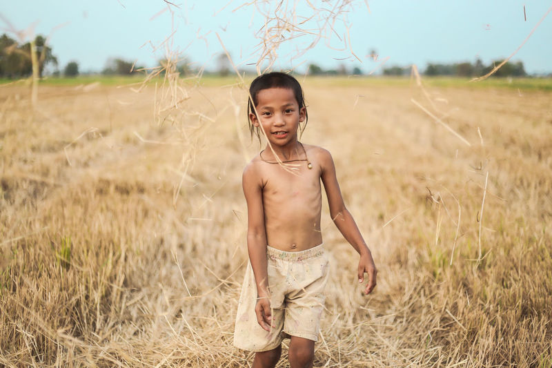 Portrait of boy throwing straws while standing on field at farm against sky