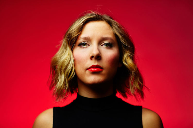 Portrait of young woman wearing lipstick against red background