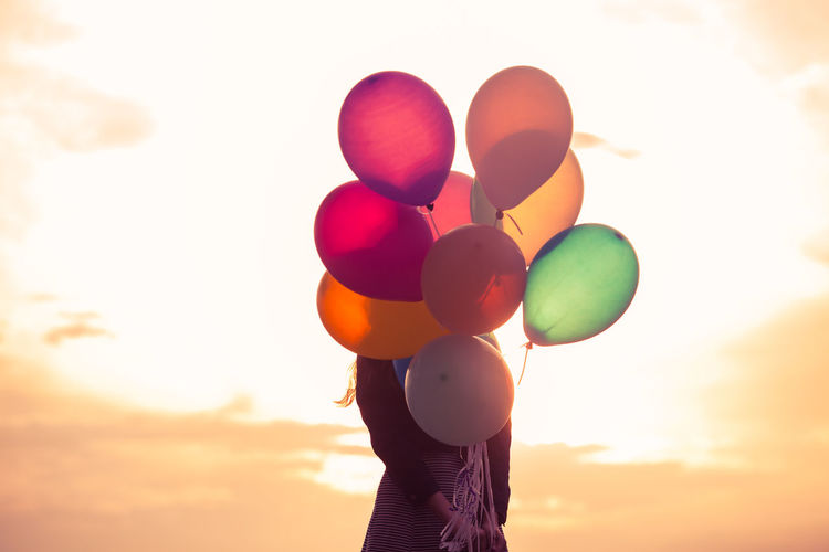 Low angle view of woman holding balloons against sky during sunset