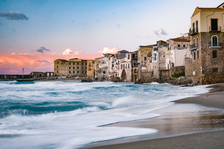 Buildings by sea against sky during sunset