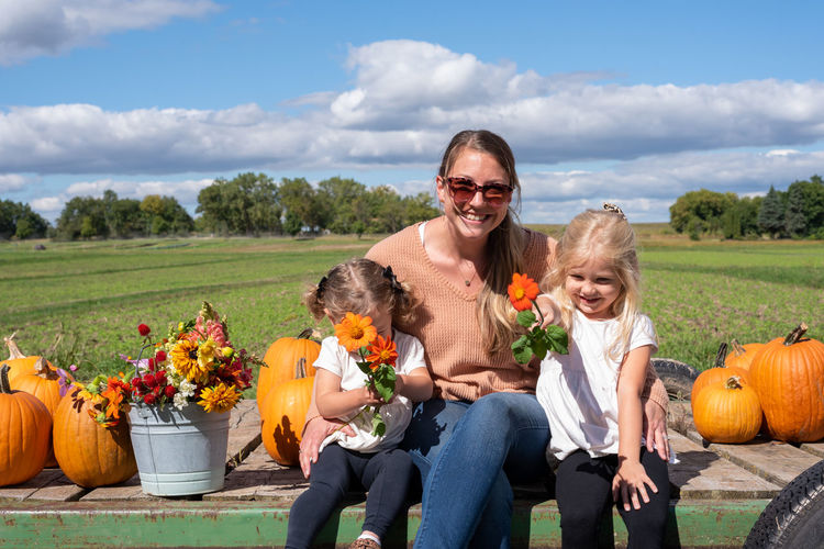 Portrait of happy mother with daughters sitting by plants against sky