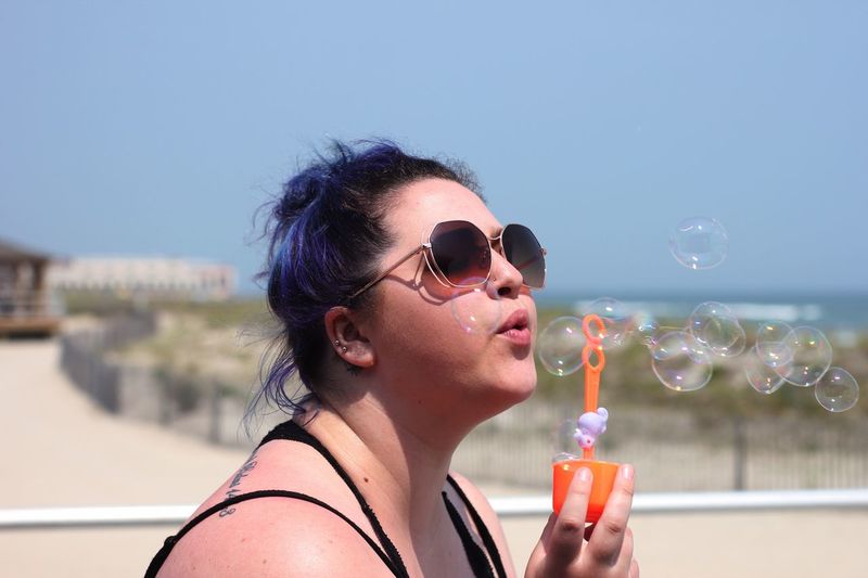 Young woman blowing bubbles at beach against sky