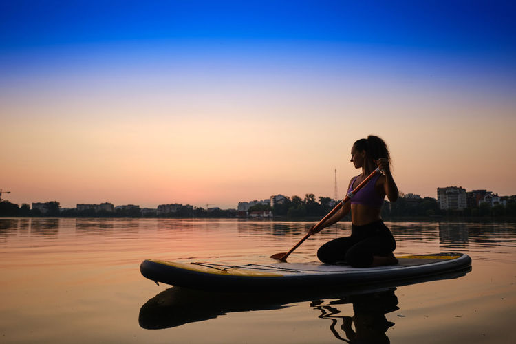 Woman sitting in boat against sky during sunset