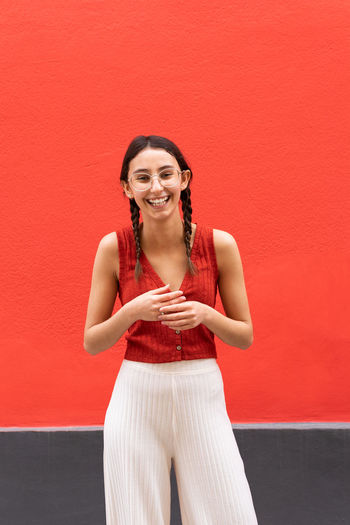 Cheerful young female in pigtails hairstyle while looking at camera on red background in street
