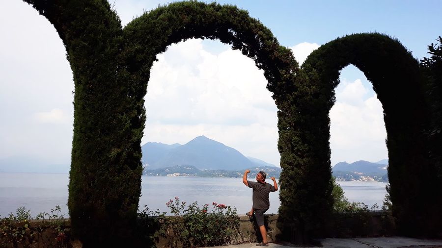 Man standing by arch made with creeper plants against sea and sky