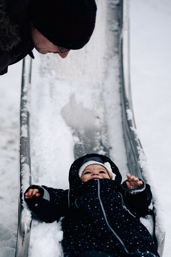 Father looking at baby girl playing on snow covered slide
