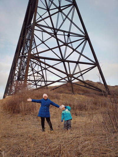 Full length of woman standing with daughter against electricity pylon