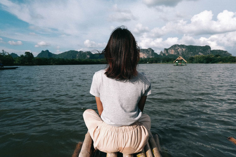 Woman sitting on wooden raft over lake against sky