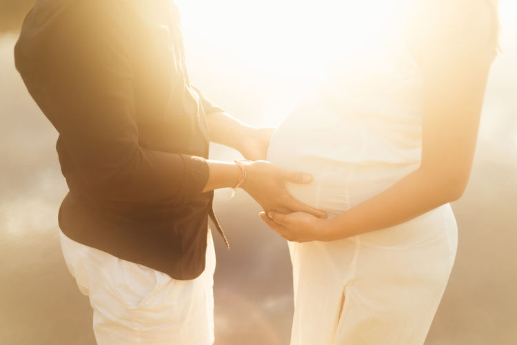 Midsection of man touching pregnant woman belly while standing outdoors during sunset