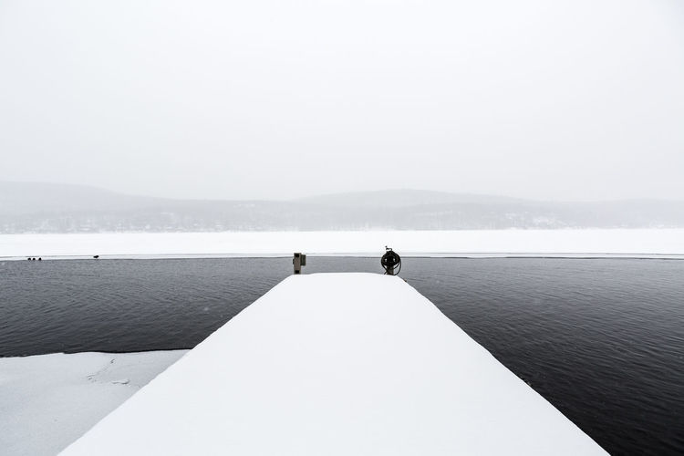 Snow covered pier by lake against sky