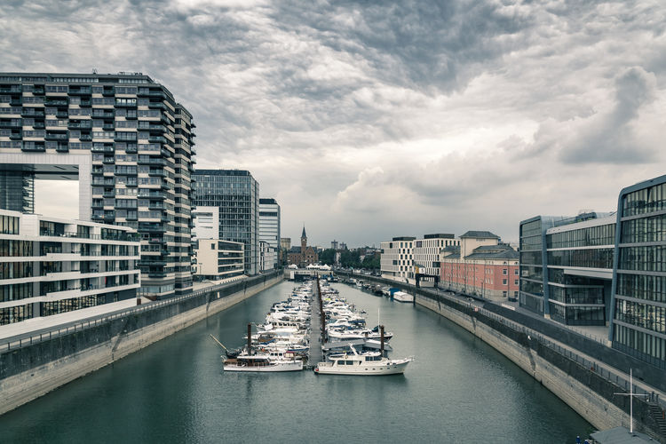 Boats in rhine river by kranhaus against cloudy sky