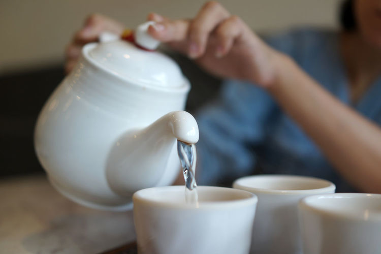 Midsection of woman pouring water in cup on table
