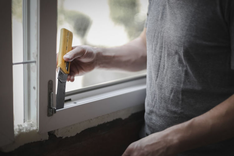 Caucasian man cleans a window frame with a construction knife.