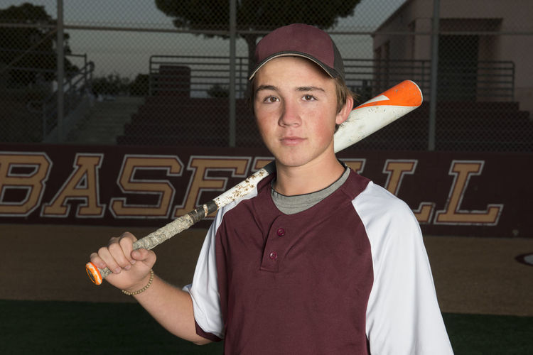 Portrait of a high school baseball player in maroon uniform holding his bat