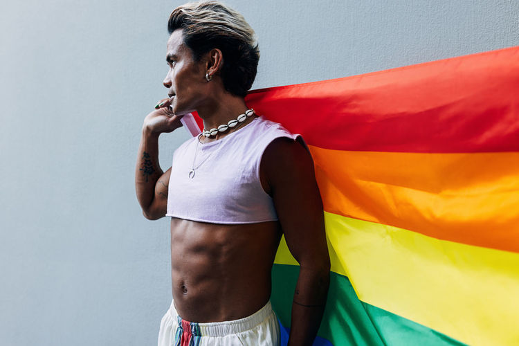 Gay man with rainbow flag against wall