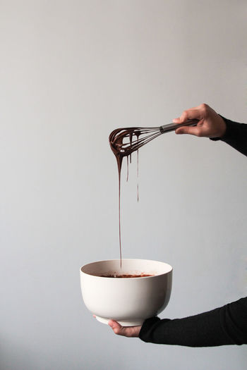 Crop view of hands of anonymous woman in black clothes, draining chocolate from a whisk into a white bowl