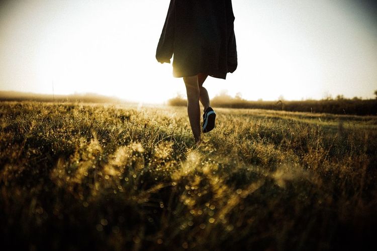 Low section of woman walking on field against clear sky during sunset