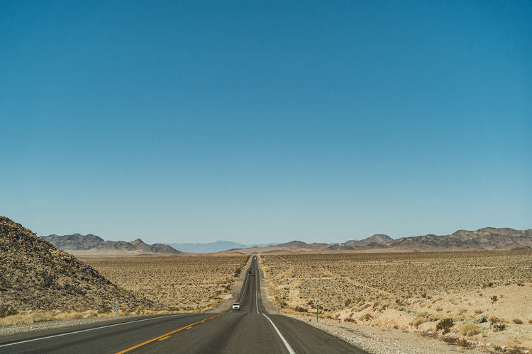 Road passing through desert against clear blue sky