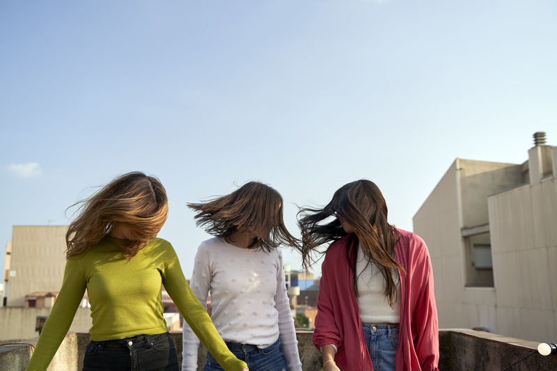 Female friends blowing hair in wind standing on building terrace