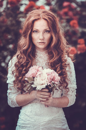 Portrait of bride holding bouquet standing outdoors