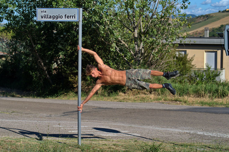 Low angle wiev of boy performs calisthenics exercises using a road sign