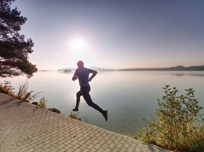 Man running on lake shore pavement during sunrise or sunset - healthy lifestyle concept