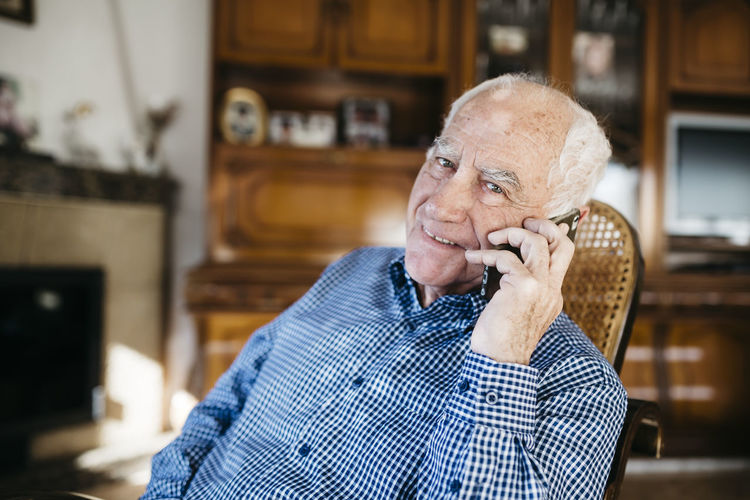 Portrait of smiling senior man telephoning with smartphone at home