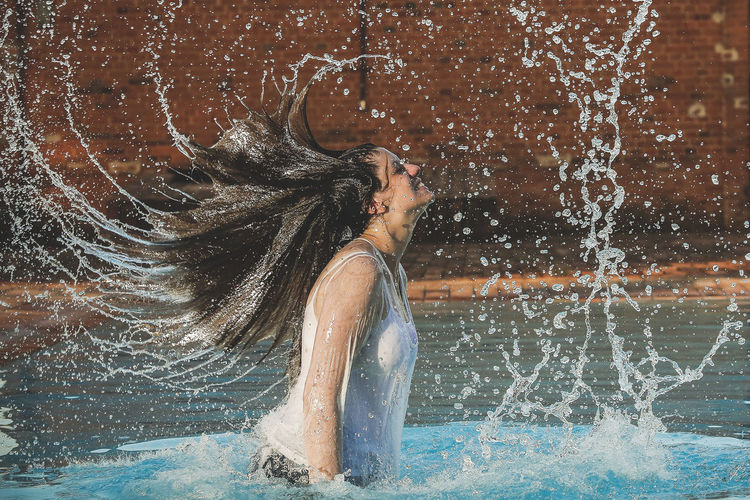 Full length of young woman splashing water at night