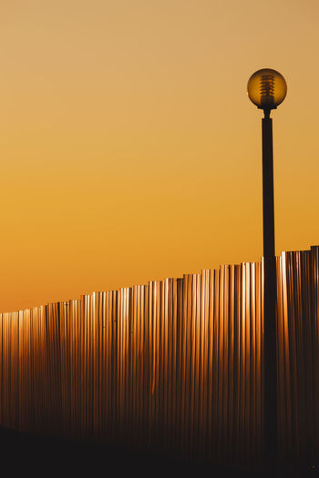 Street light by a metal fence against clear sky during sunset