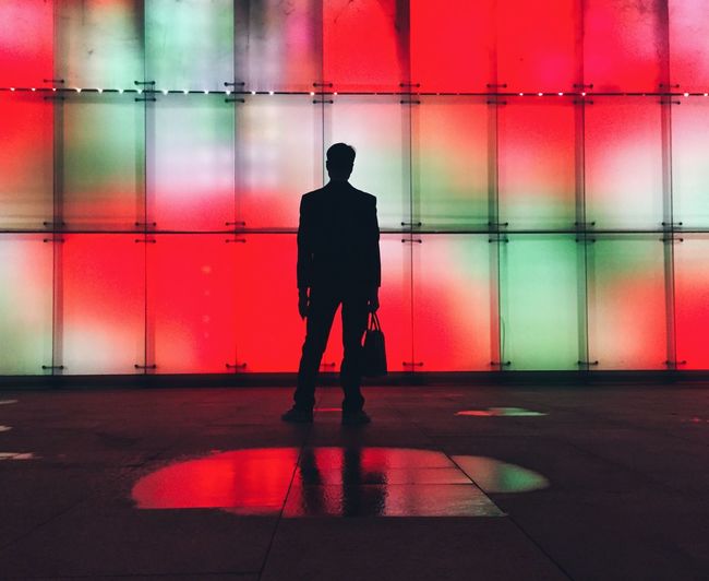 Silhouette man standing against illuminated wall at night