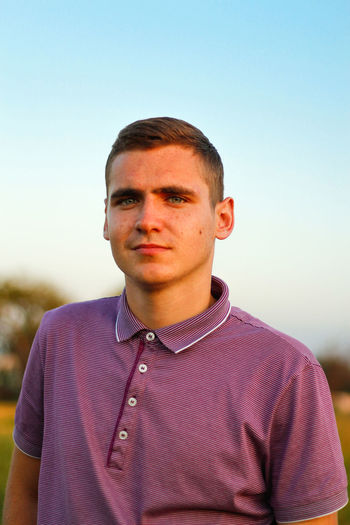 Young people.portrait of serious young brunette man in purple polo shirt standing outdoor on nature 