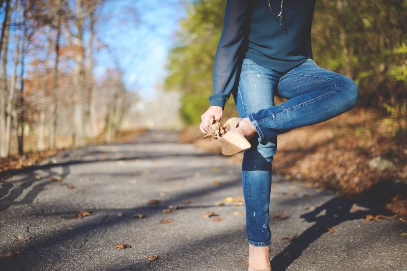 Woman pulling leaves from her high heels on street