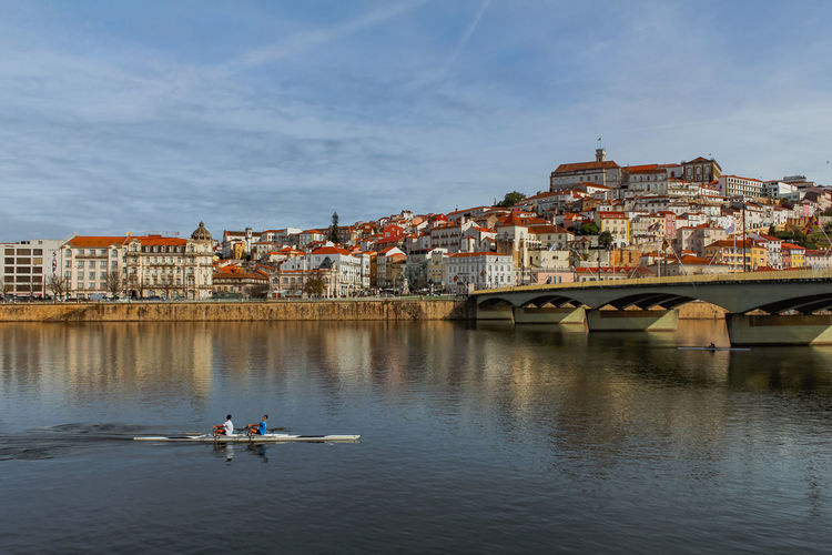  bridge over mondego river with rowing k2 by buildings in coimbra view against sky