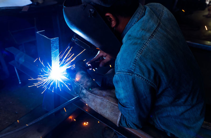 Welder welding metal with argon arc welding machine and has welding sparks. a man wears welding mask