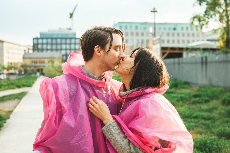 Young couple wearing pink raincoat while kissing in city
