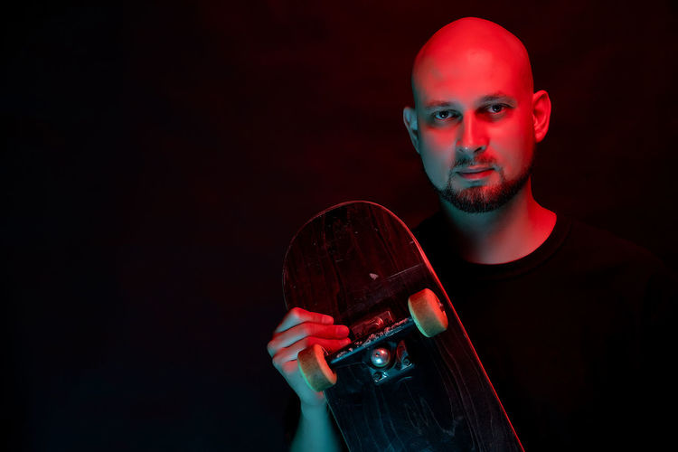 Portrait of man with skateboard against black background