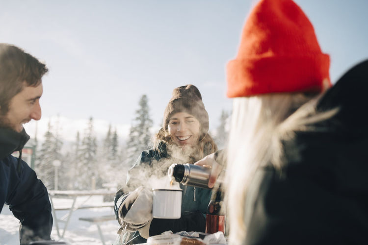 Young woman pouring coffee for female friend during winter