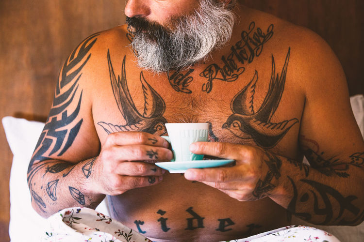 Midsection of tattoed man drinking a cup of coffe