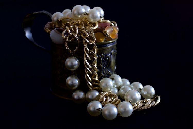 Close-up of pearl necklace in container against black background
